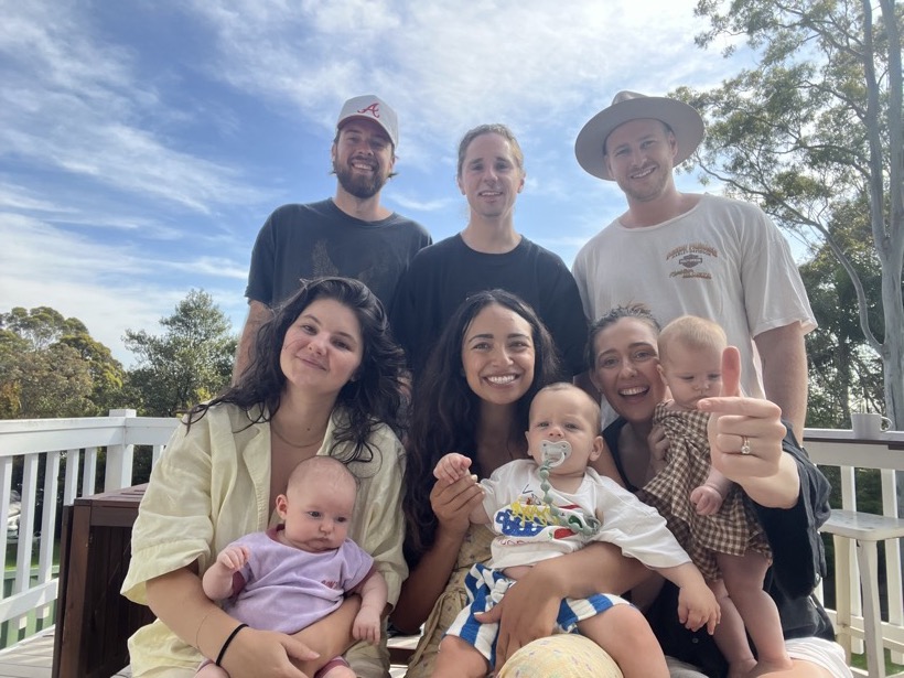 Friends and family gathered outside with babies, smiling together.